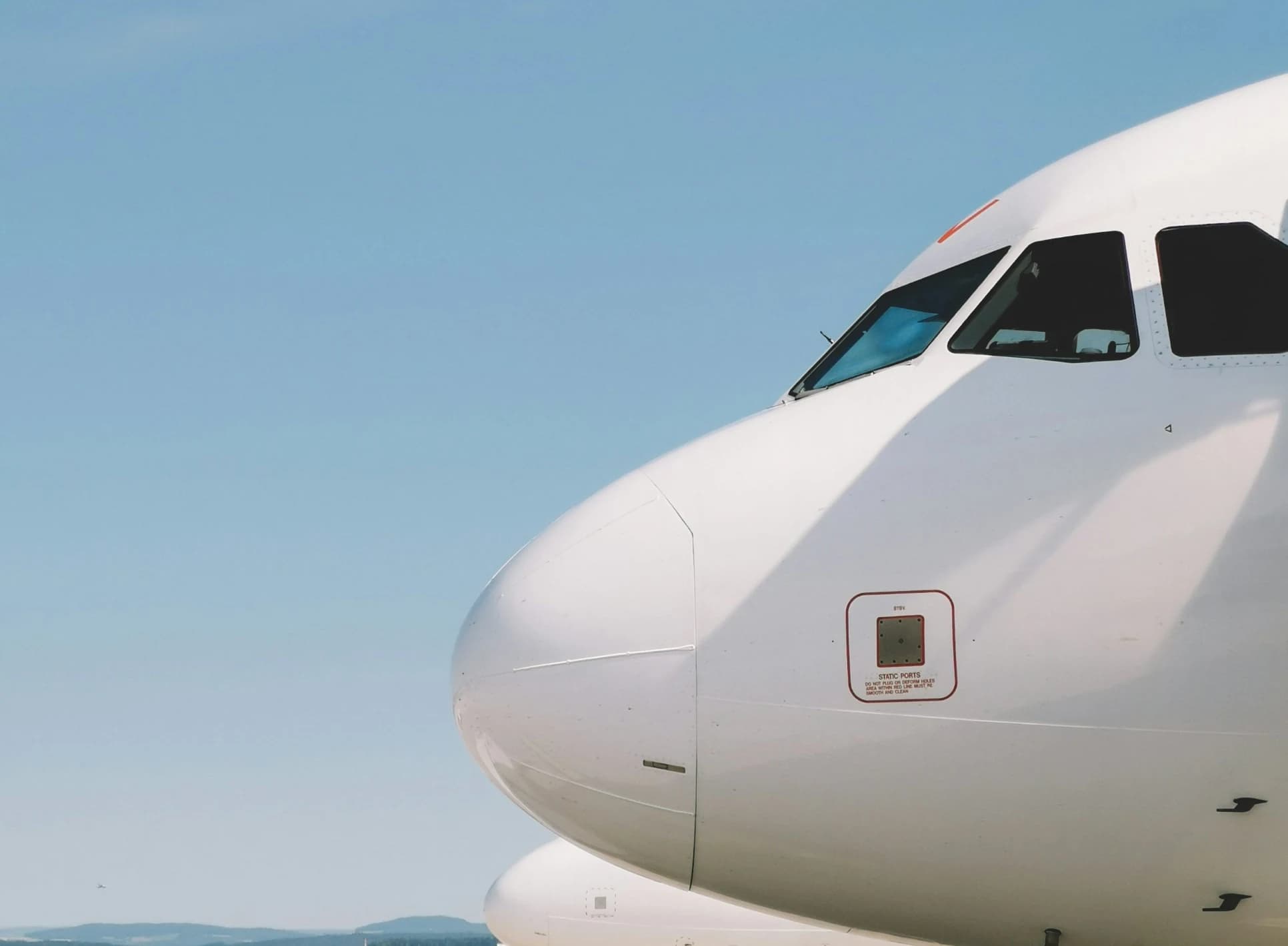 Nose of a white airliner at the gate under a clear blue sky