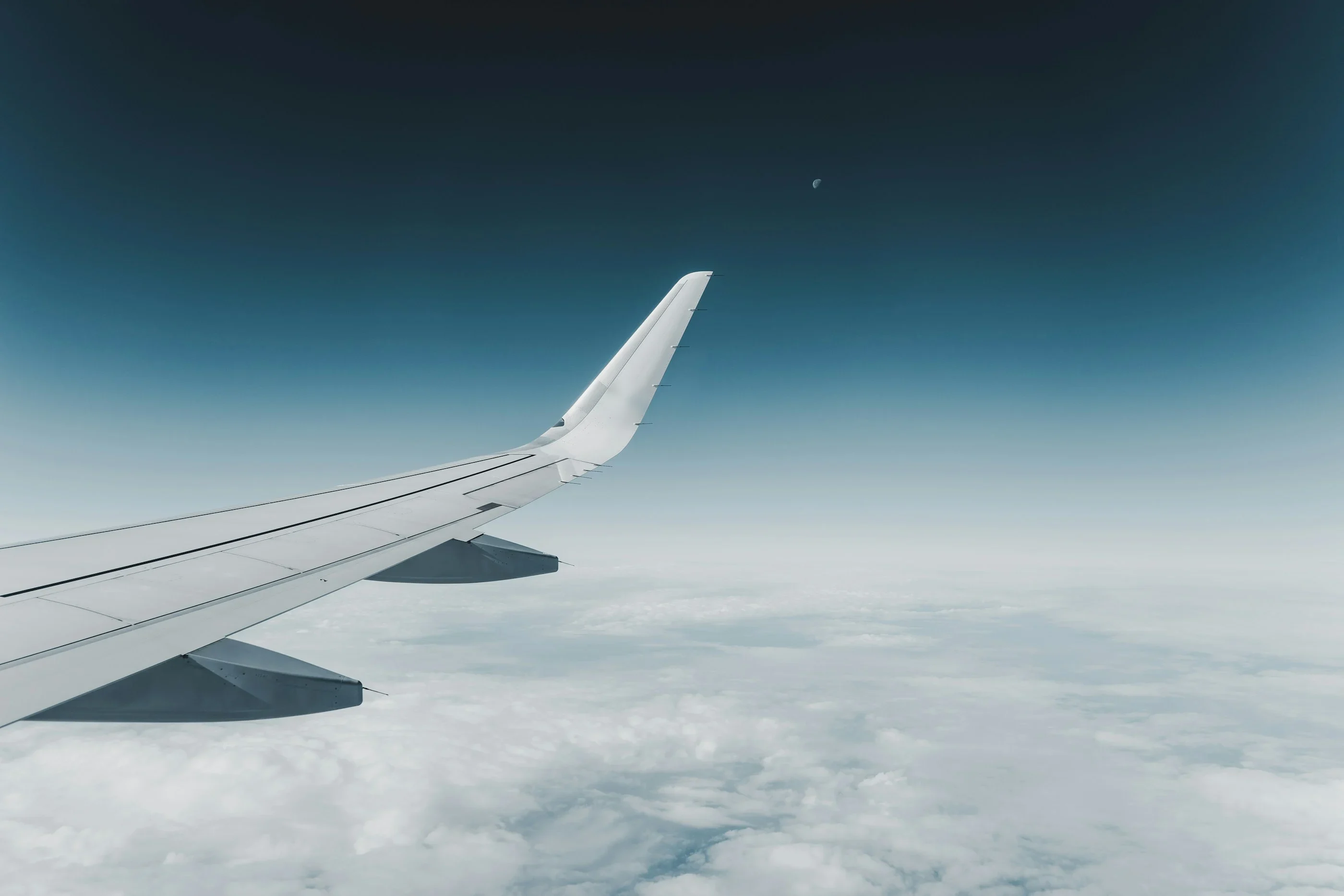 An airliner wing over a sea of cloud at blue hour