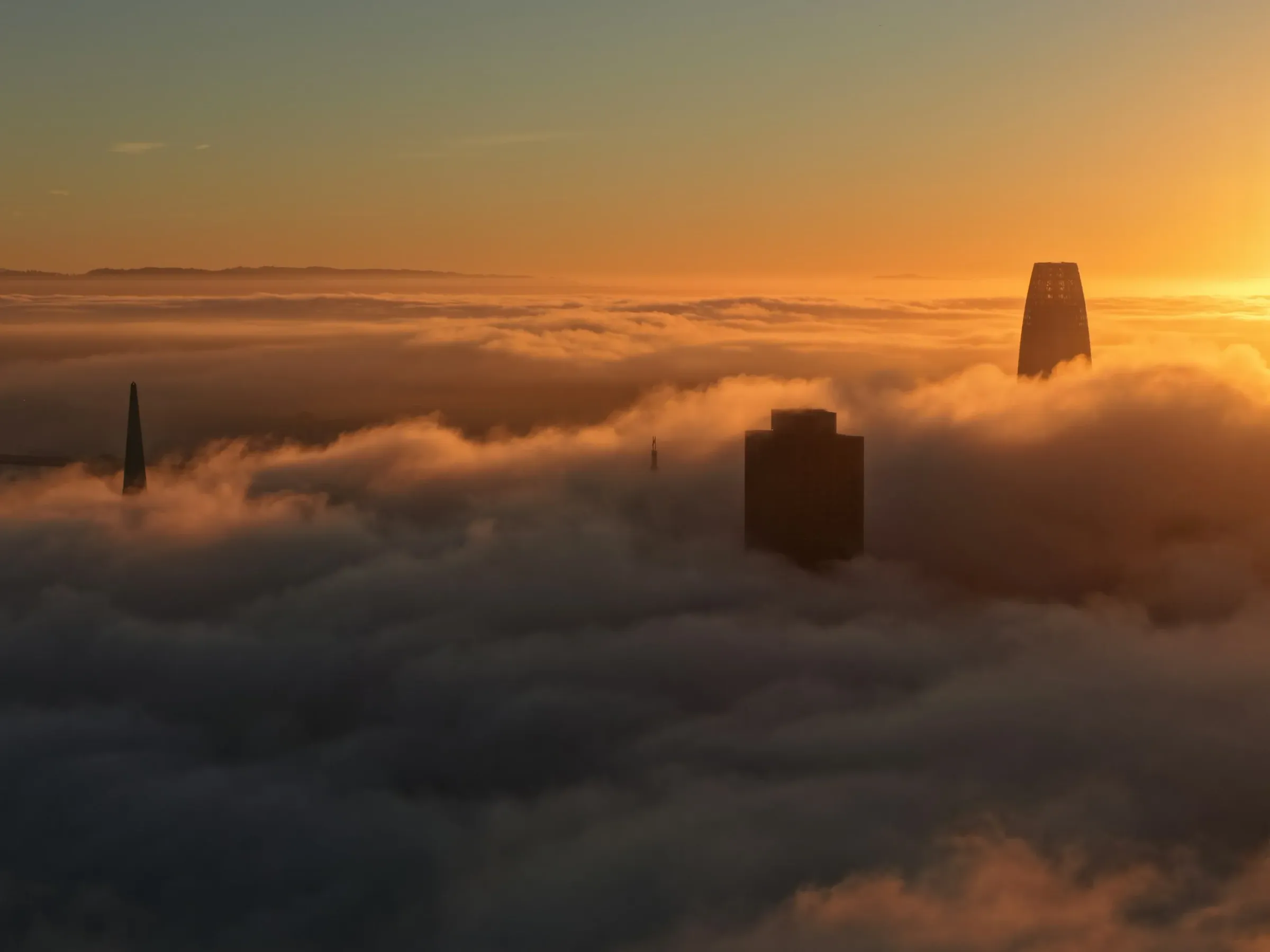Skyscrapers rising out of a sea of clouds at sunset