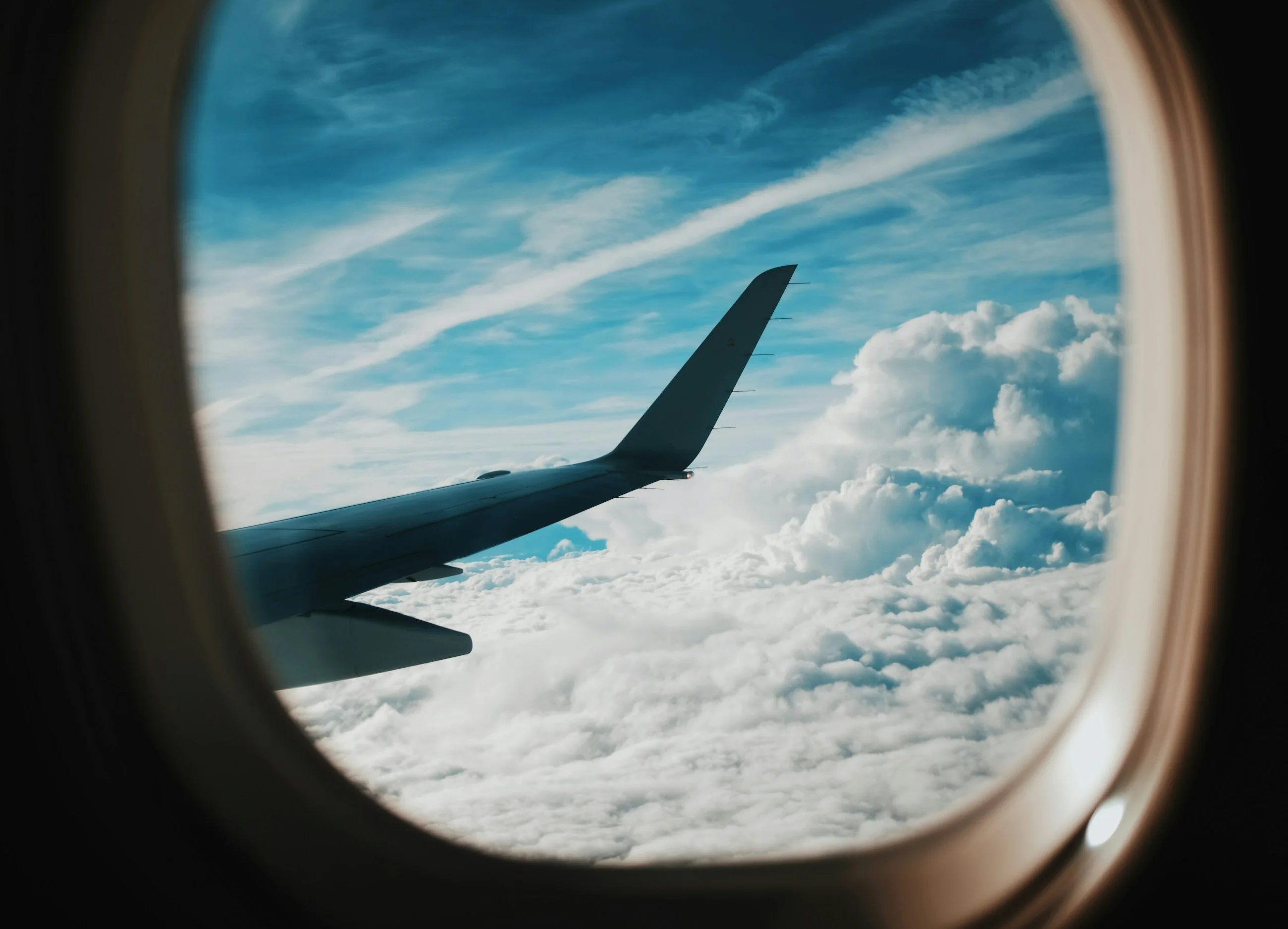 An aircraft wing above bright cumulus clouds, seen through a cabin window