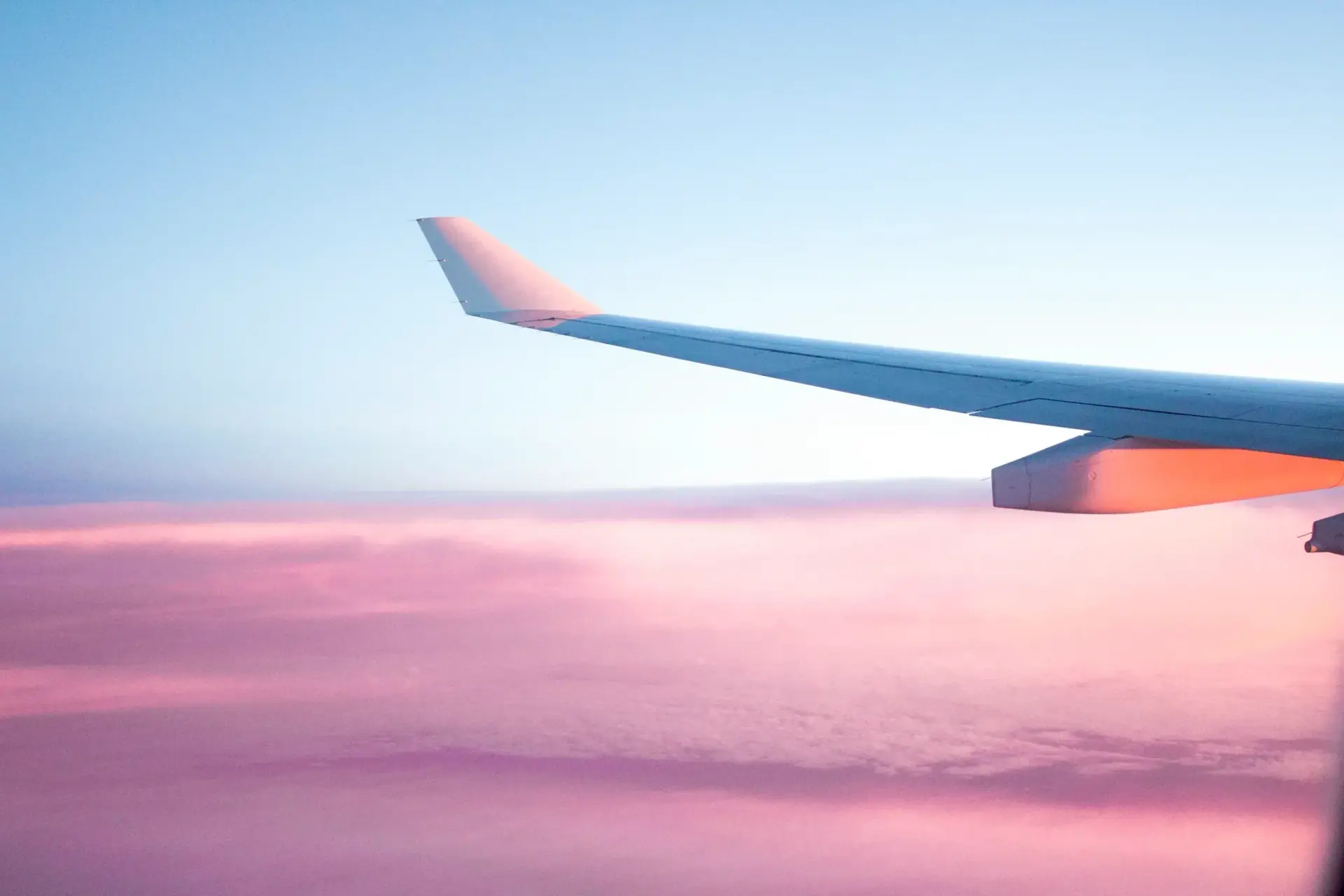 An airliner wingtip above a sea of pink clouds at dawn